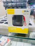 A boxed portable power bank on a glass display shelf. The packaging is white and yellow with a photo of a black square power bank and a red wrist strap, and text including “ΑΠΩL Gold,” “22.