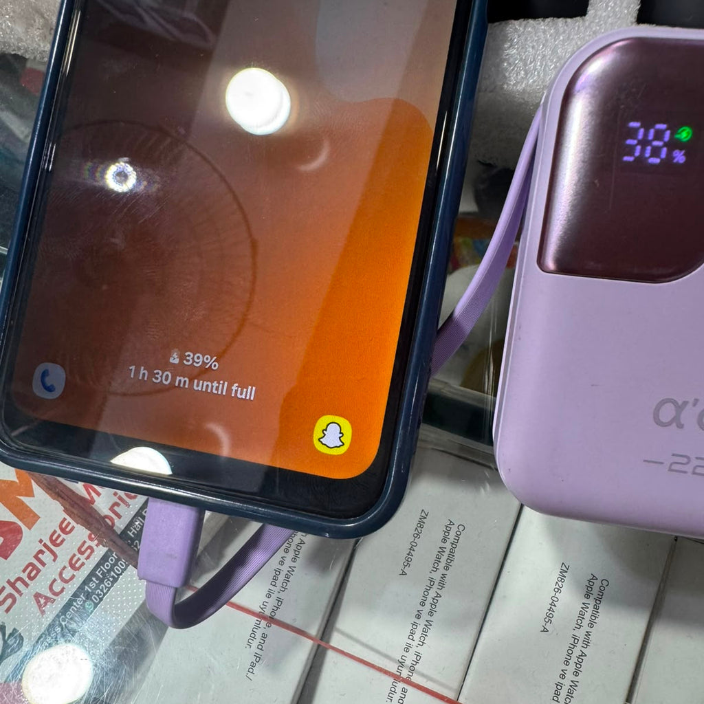 A close-up of a light purple portable power bank with a digital display showing 38% battery, next to a smartphone with a purple cable, resting on white product boxes.
